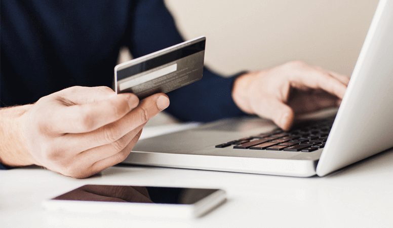 A close-up of somebody holding a bank card, with a laptop and mobile phone