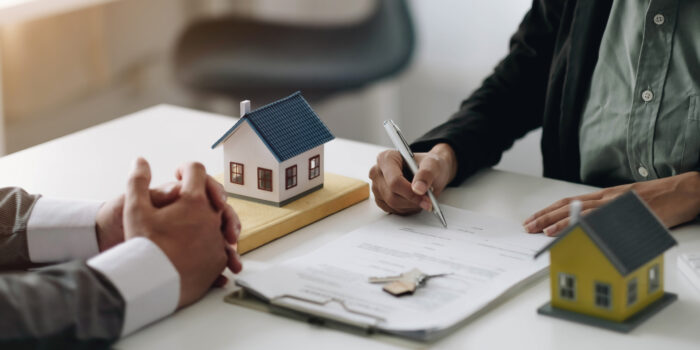 Real estate agents explain the document for customers who come to contact to buy a house, buy or sell real estate concept two people sitting across a desk, signing fincancial documents.