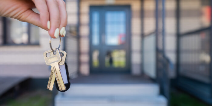 A woman holds the keys to a new house. Close-up of a female hand. Buying a property. A hand holding a pair of house keys