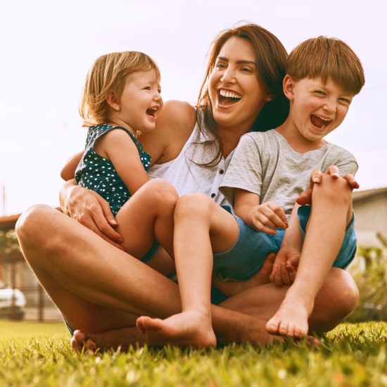 Mother and children sitting on grass and laughing.