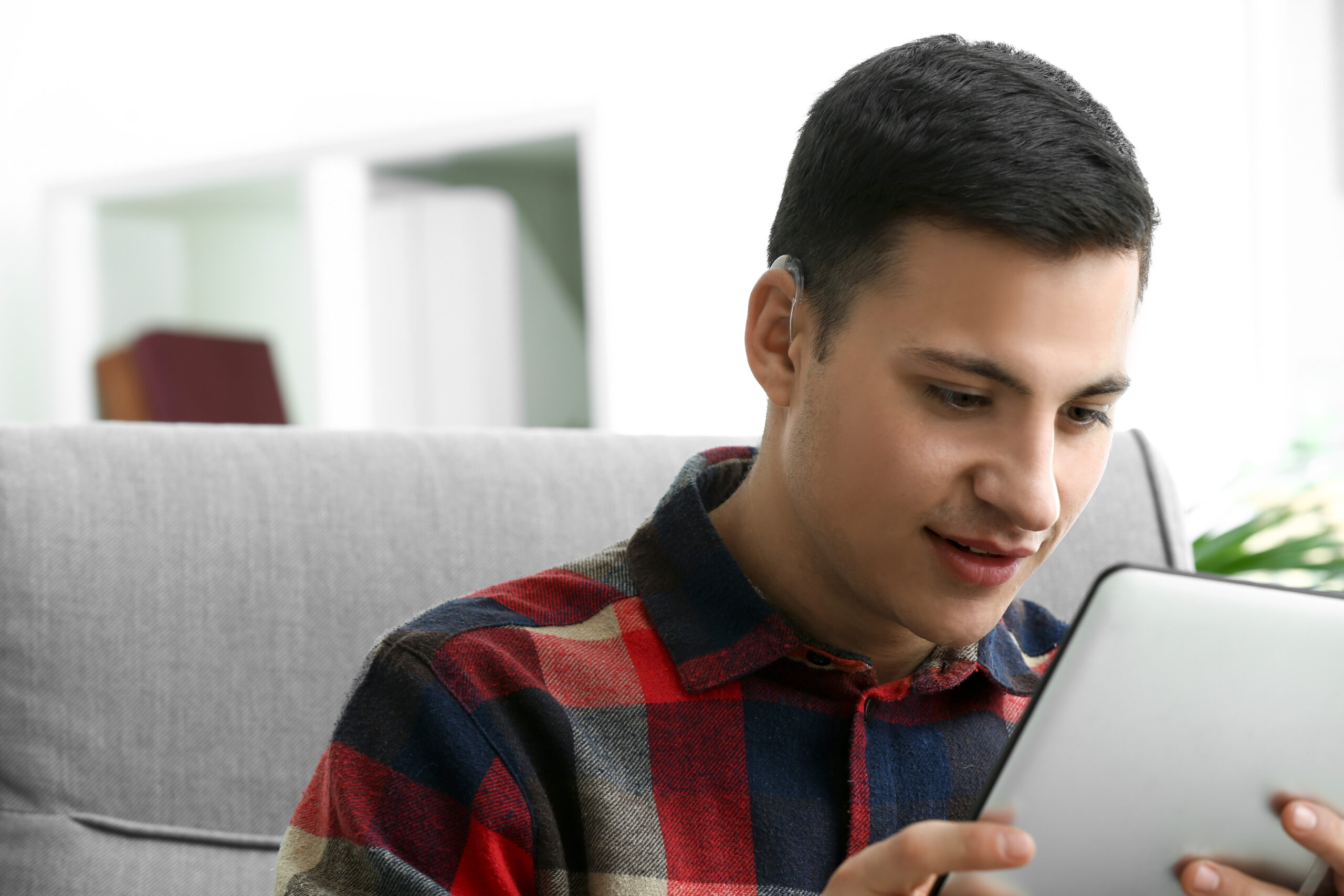 Young,Man,With,Hearing,Aid,Using,Tablet,Computer,At,Home Young,Man,With,Hearing,Aid,Using,Tablet,Computer,At,Home